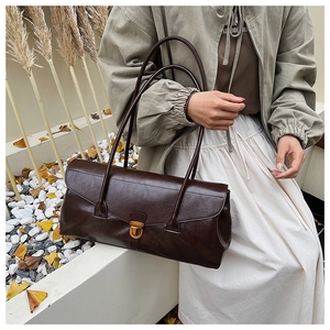 Detail of dark brown retro baguette bag with glossy texture and gold buckle closure