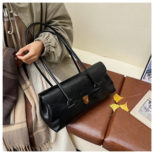 Close-up of black leather baguette bag with bronze snap lock on a vintage leather bench