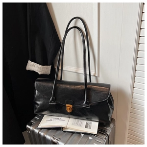 Detail of vintage black leather shoulder bag with gold metal buckle in office setting
