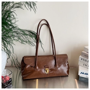 Close-up of vintage brown leather baguette bag with a metallic gold buckle on a desk