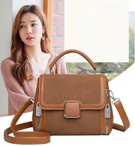 Detailed close-up of brown textured leather handbag with square metal buckle and side zippers
