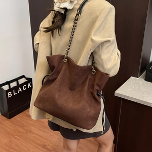 Deep brown suede bucket bag with gold chain strap shown from a model's back perspective