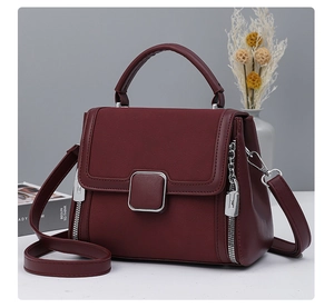 Detailed view of burgundy leather handbag with silver square buckle and side zipper accents