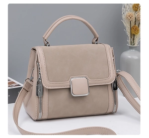 Detail view of beige handbag with metal buckle and mixed leather texture in soft studio lighting
