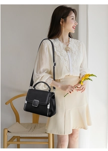 Close-up of black leather handbag featuring a silver square twist lock and decorative zippers