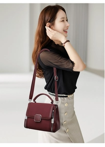 Model wearing a burgundy faux leather handbag with silver clasp and side zipper detail