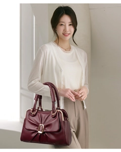 Detailed view of wine red pleated leather handbag with golden buckle held by a model