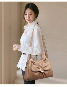 Detailed view of tan pleated shoulder bag with gold buckle on a model in white shirt