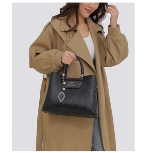 Détail d'un sac à main noir gaufré avec poignée tressée et breloque feuille en métal