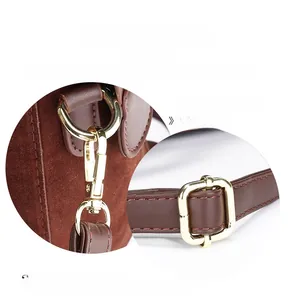 Detailed macro view of gold-tone metal buckles and hooks on dark brown suede handbag
