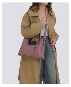 Détail du sac à main en cuir rose poudré avec poignée tressée et pendentif feuille