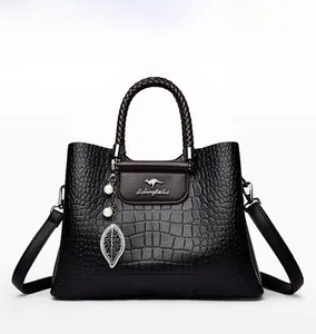 Détail du sac à main noir en cuir de crocodile avec anses tressées et pendentif perle feuille