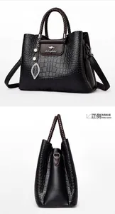 Détail de motif crocodile sur sac noir avec poignées tressées et pendentif feuille