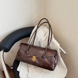 Retro dark brown leather baguette shoulder bag with gold clasp on a cozy white jacket