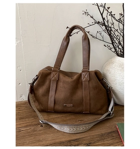 Macro detail of brown suede tote bag featuring a textured strap and metal logo plaque