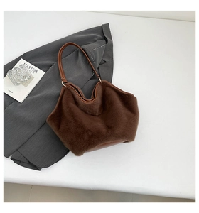 Close-up of fluffy dark brown plush tote bag with faux leather strap on grey blazer