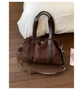 Detail of suede boston bag in dark brown with textured woven strap on indoor rug
