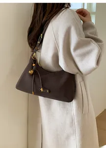 Detail of vintage dark brown leather underarm bag with gold charm and buckle on white coat
