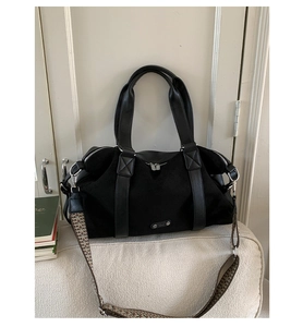 Close-up of large black suede tote bag with geometric patterned strap on white sofa