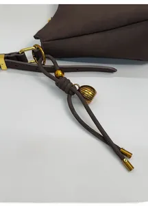 Close-up of dark brown leather bag with golden metal rings and delicate tassel charms