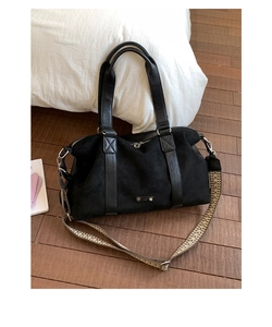 Detail of black suede tote bag with woven geometric shoulder strap on wooden floor
