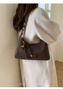 Detail of dark brown suede shoulder bag with gold sphere charm and metal logo tag