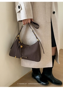 Detail of dark brown leather underarm bag with gold hardware and woven knot charm