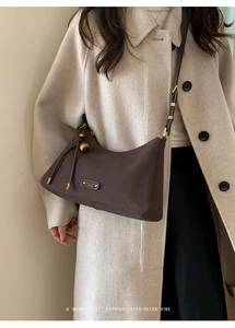 Detail of dark coffee underarm bag showing metal logo and gold-tone buckle on wool coat