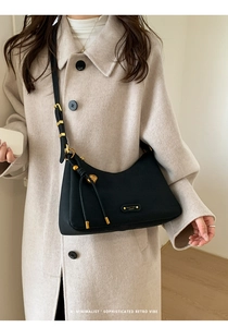 Close-up of black matte leather hobo bag with gold logo plaque and long tassel detail