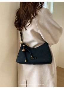 Close-up of black retro underarm bag with gold metal spherical charm and brand nameplate