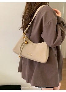 Detail of beige crescent underarm bag with gold ball charm and metallic logo on leather