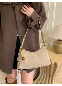 Detail of minimalist beige faux suede shoulder bag with gold hardware and tassel
