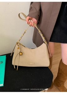 Detail of beige suede shoulder bag with golden hardware and spherical pendant
