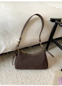 Detail of dark brown hobo bag with matte texture and gold buckle on white bedding
