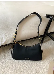 Close-up of matte black leather underarm bag with gold metal zipper and adjustable buckle