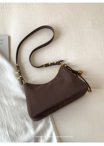 Detailed close-up of retro brown leather shoulder bag with golden bell charm and buckle