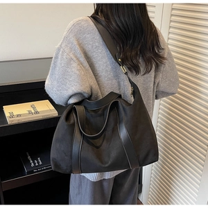 Detail of large black suede tote bag with leather straps and gold metal hardware