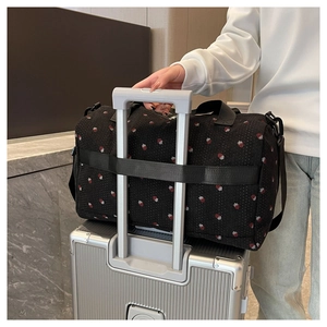 Detail showing the trolley sleeve of a black strawberry print travel duffel bag on luggage
