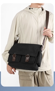 Detail view of men's black canvas messenger bag with brown leather straps and metal rivets