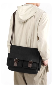 Rear view of black canvas messenger bag with brown leather accents on a male model