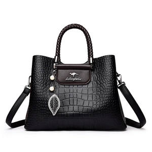 Sac à main noir gaufré crocodile avec poignée tissée et pendentif perle sur fond blanc