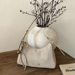 Vintage beige suede underarm bag with gold hardware and tassel on a rustic wood table
