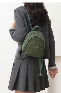 Detail of dark green corduroy mini backpack on a model in a casual gray outfit