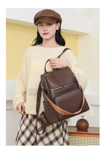 Detail view of brown PU leather backpack with decorative orange strap and zip pockets