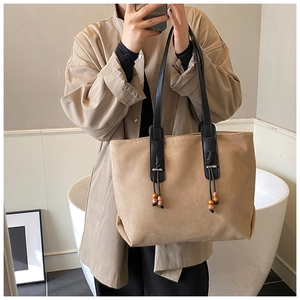 Dettaglio della grande borsa tote beige con cinturini neri e nappe con perline su un modello