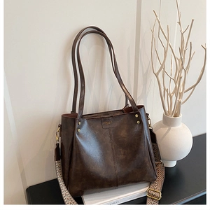 Detail of vintage brown textured leather bag with colorful woven shoulder strap and logo