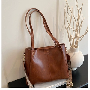 Detail of vintage brown leather bag showing wide geometric fabric strap and metal rivets