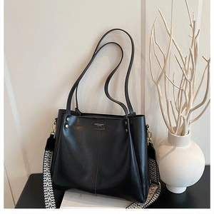 Detail view of large black tote bag with textured leather and wide woven shoulder strap