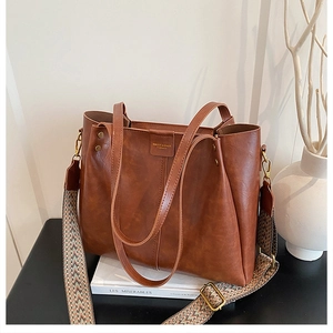 Detail of a large brown leather tote with a retro geometric woven wide strap and gold hardware