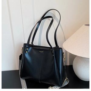 Detail of black tote bag featuring wide geometric woven strap and gold rivet accents